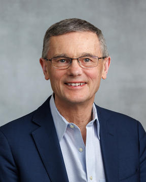 an image of John Campbell, in a navy blazer with glasses